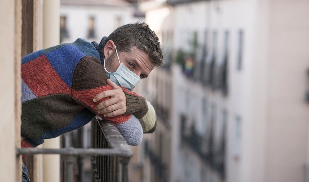Ein Mann lehnt an einem Balkon mit Maske auf. Südländisches