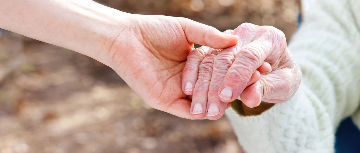 Hand eines Pflegers hält Hand einer Pflegebedürftigen